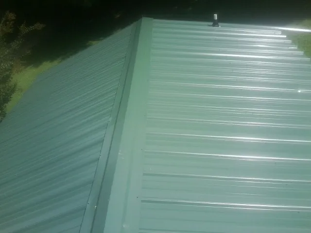 New green metal panels meeting at the ridge of a roof — Flat Roof Repair work by our crew in Lyons